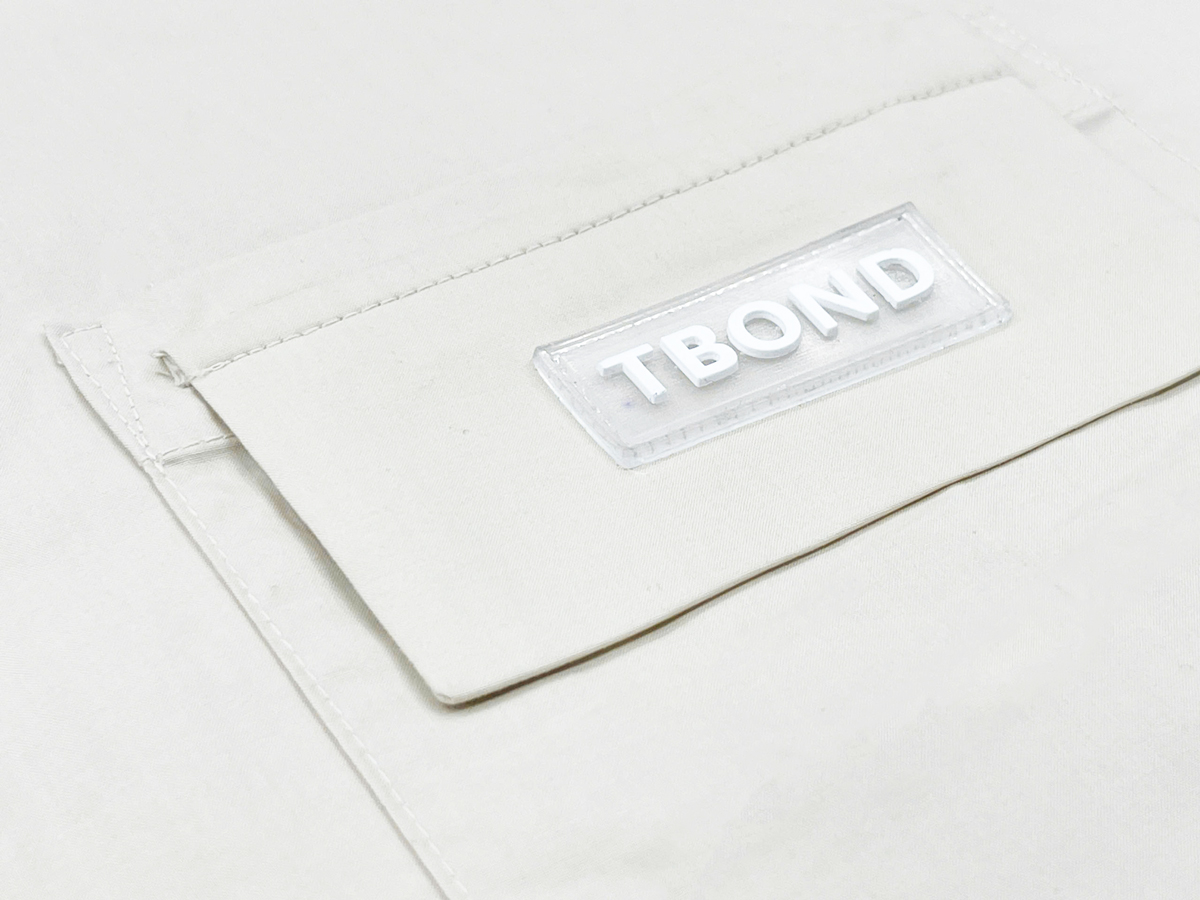 The TBOND tag features a transparent plastic base with embossed lettering, creating a striking 3D effect.
